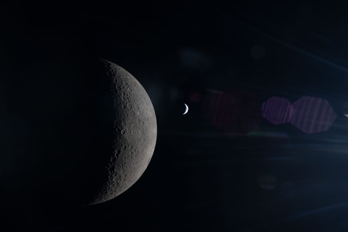 The partly lit gray Moon on the left with a much smaller crescent Earth to its right against black space, with faint reflections of a spacecraft window