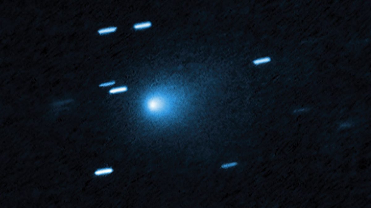 Hubble image of comet 3I/ATLAS: a bright blue-white core inside a teardrop-shaped cloud of dust on a dark background, with short bright streaks from background stars