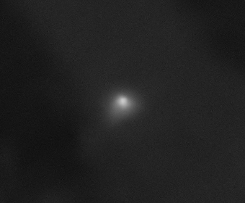 A small fuzzy white glow, the comet 3I/ATLAS, against a dark gray background in an image from the HiRISE camera on the Mars Reconnaissance Orbiter