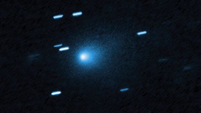 Hubble image of comet 3I/ATLAS: a bright blue-white core inside a teardrop-shaped cloud of dust on a dark background, with short bright streaks from background stars