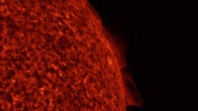 The Sun's glowing edge in extreme ultraviolet light, with a looping prominence rising from the surface into dark space